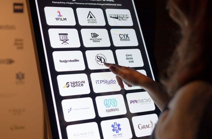 Osoba klika w logotyp znajdujący się na monitorze infokiosku. Osoba klika w logotyp znajdujący się na monitorze infokiosku.